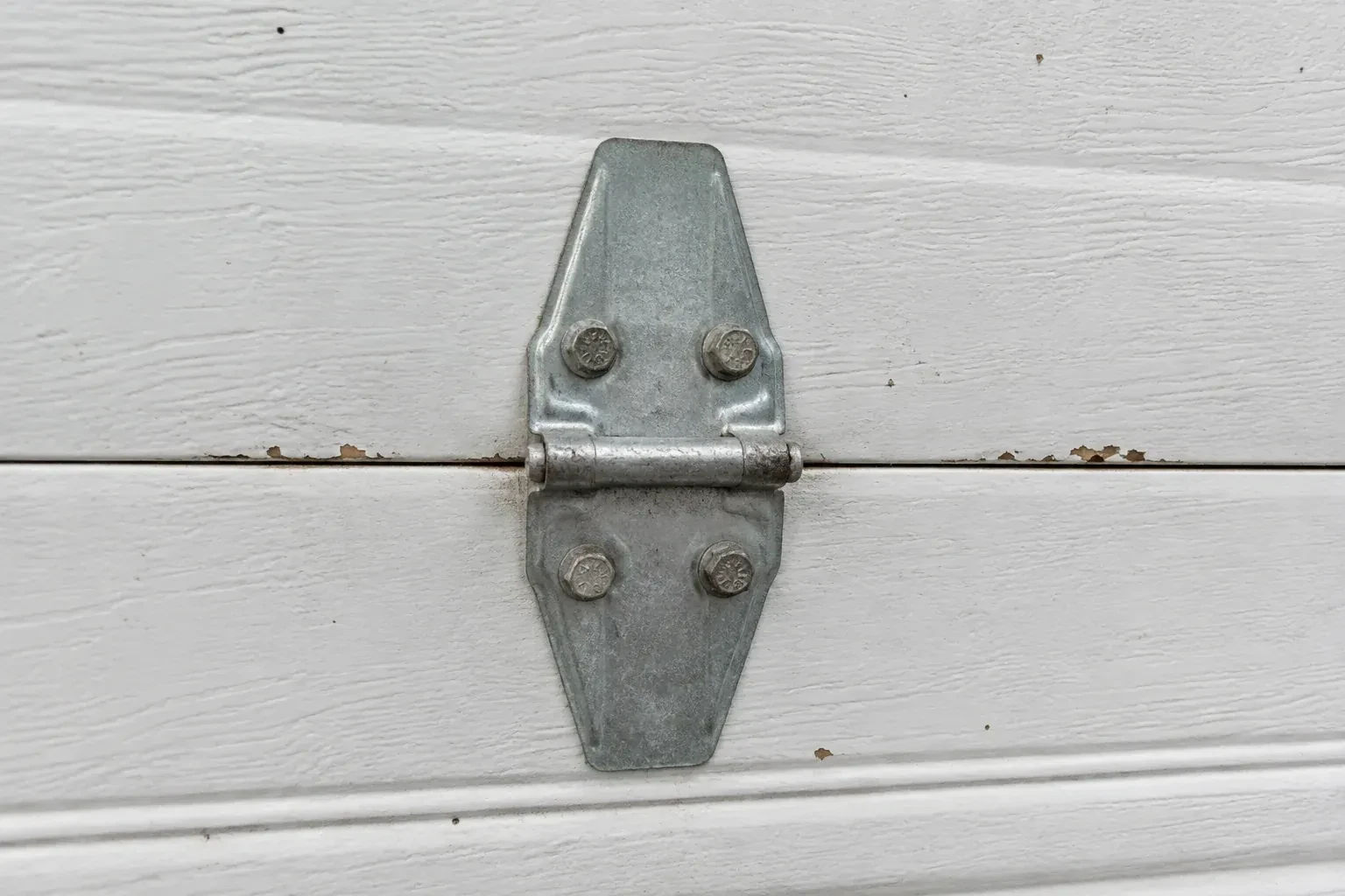 Metal center hinge across a seam in a white sectional garage door. — Garage Door Hinge Replacement, King