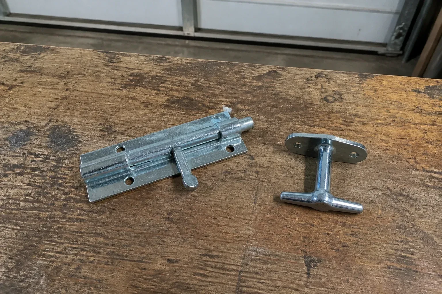 Detached slide bolt and T-handle on a wooden garage workbench. — Garage Door Manual Lock Repair, Nobleton